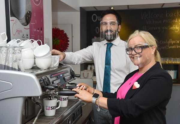 Part time lecturer Tim Smith looks on whilst Julie Curry from The Daily Apron prepares a coffee at a barista machine.